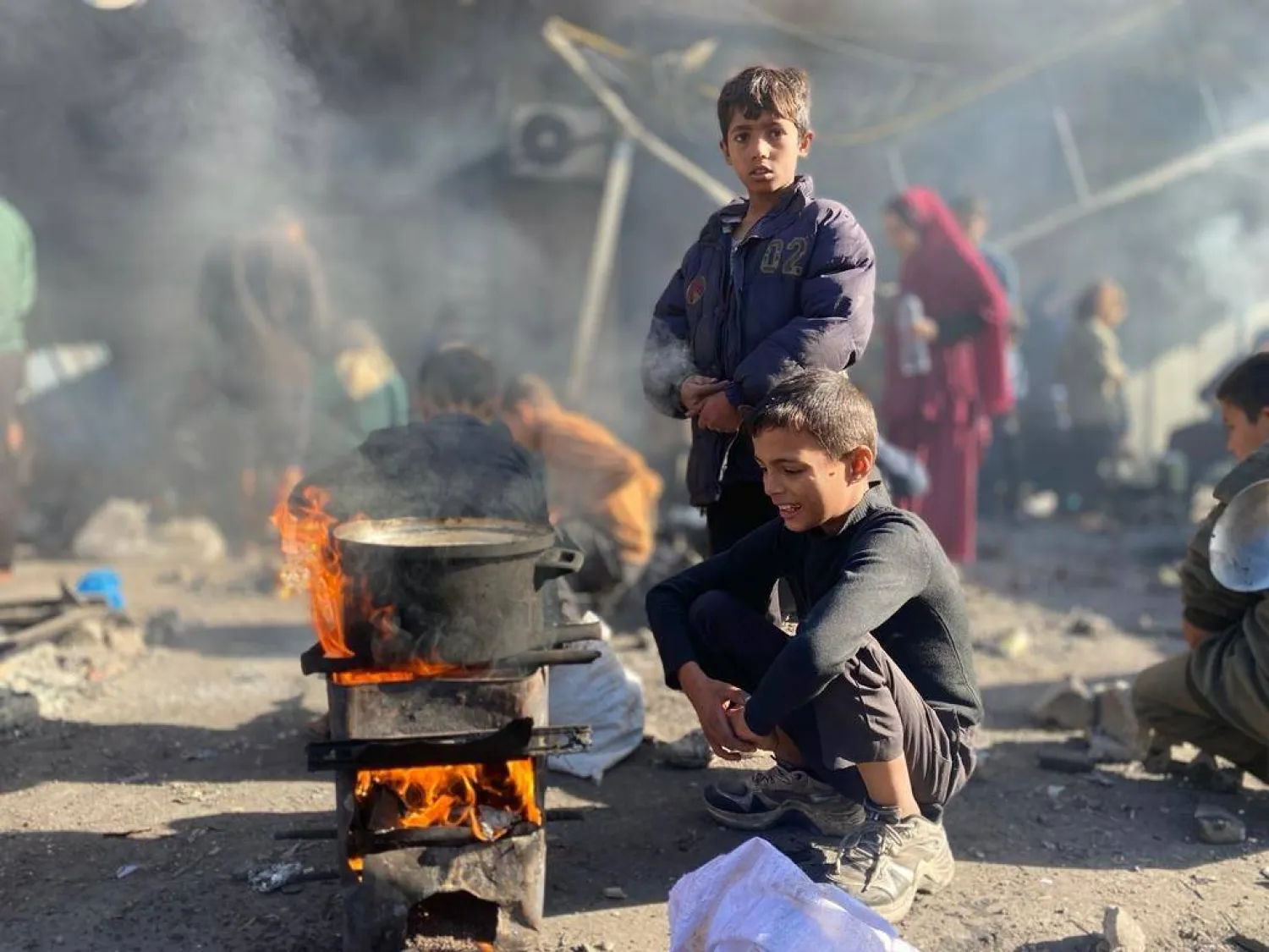طفلان فلسطينيان يطهيان على الحطب في أحد مخيمات النازحين في قطاع غزة (حساب وكالة أونروا على إكس)