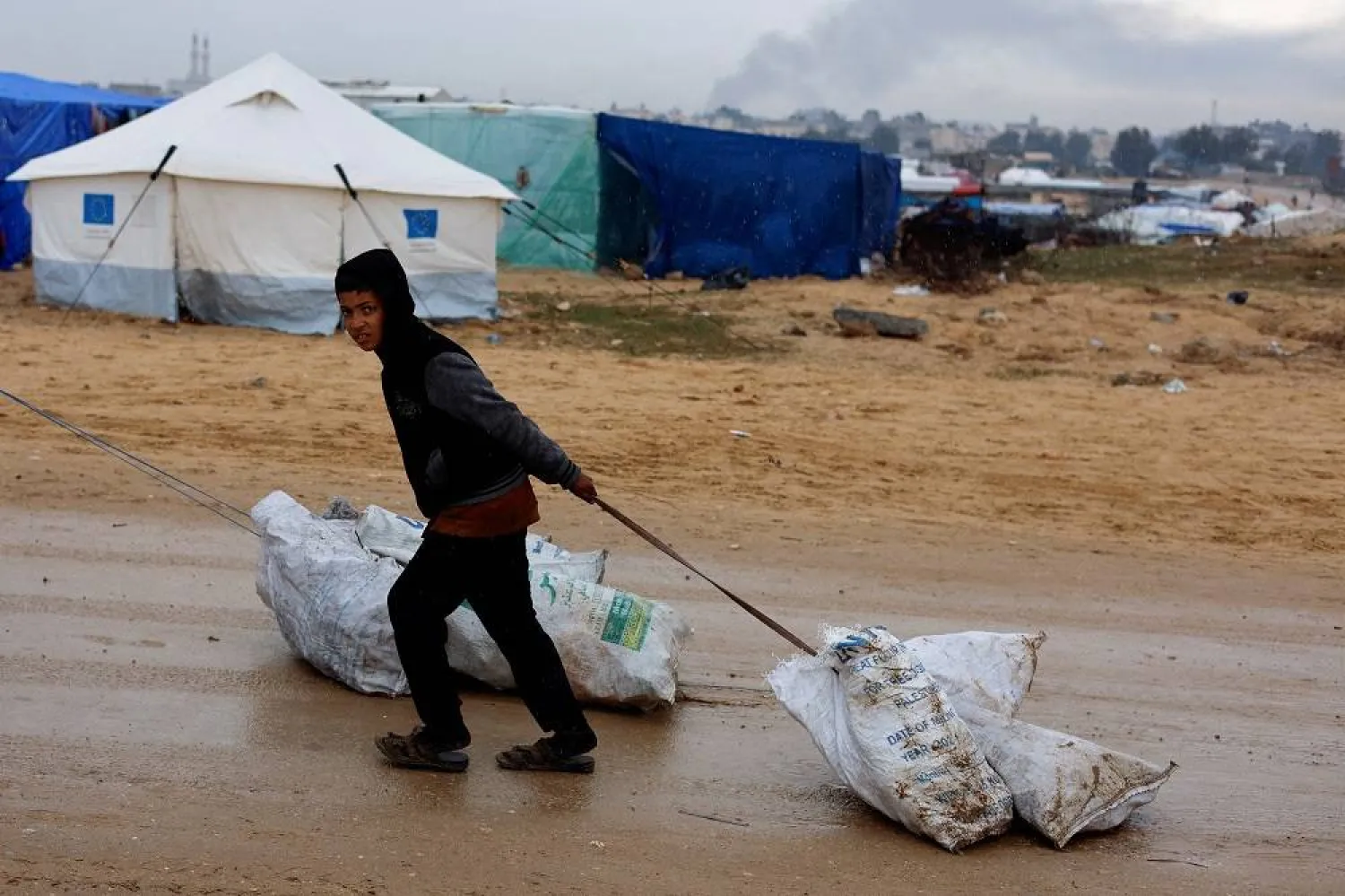 A boy pulls a bag as smoke rises in the background during an Israeli ground offensive in Khan Younis, amid the ongoing conflict between Israel and Palestinian group Hamas, as seen from Rafah, southern Gaza Strip January 29, 2024. (Reuters)
