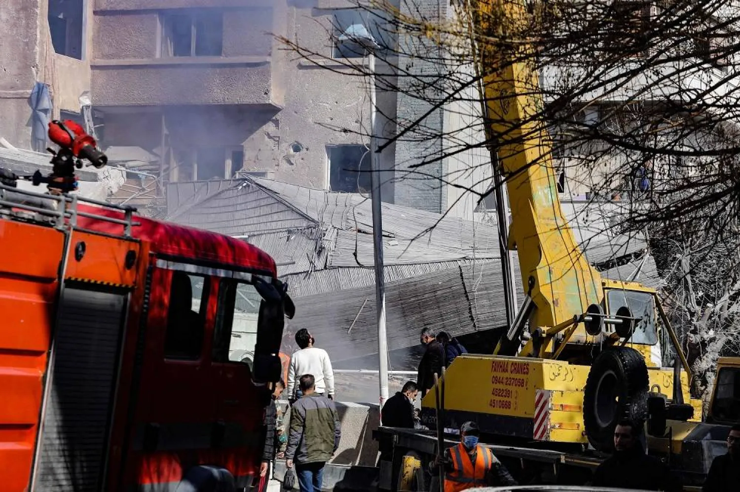 People and rescuers gather in front of a building destroyed in a reported Israeli strike in Damascus on January 20, 2024. (AFP)
