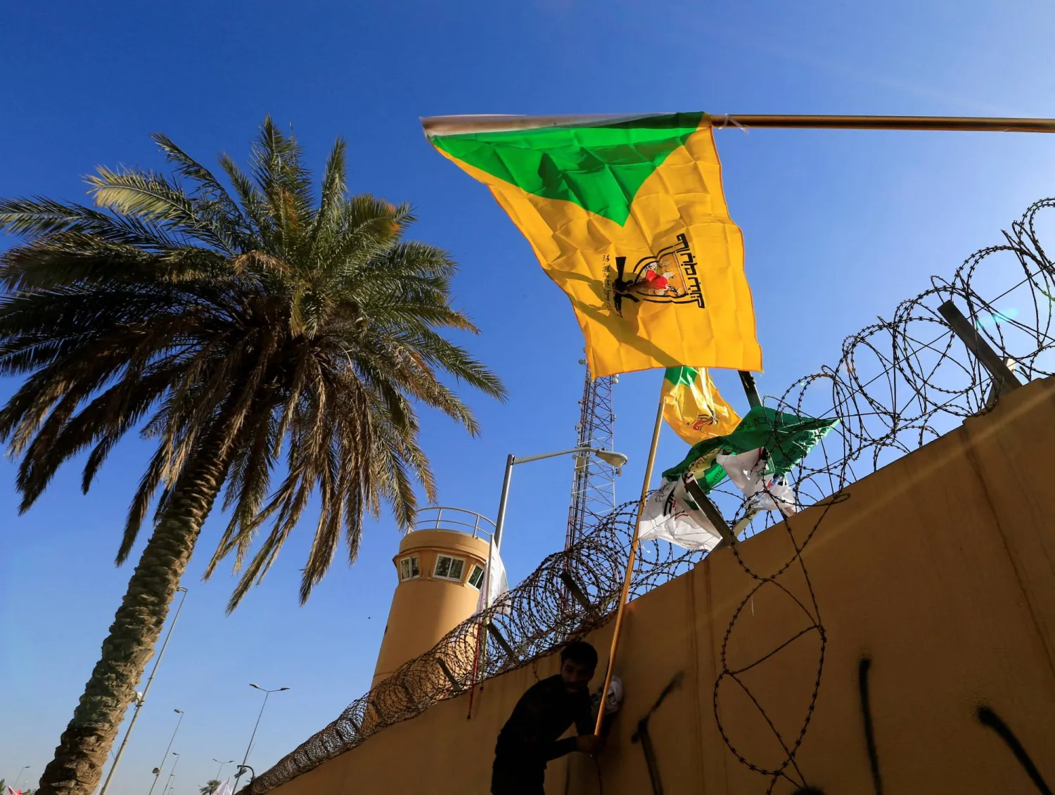 FILE PHOTO: A member of the Popular Mobilization Forces holds a flag of the Kataib Hezbollah group during a protest to condemn air strikes on their bases, outside the main gate of the US Embassy in Baghdad, Iraq December 31, 2019. REUTERS/Thaier al-Sudani/File Photo