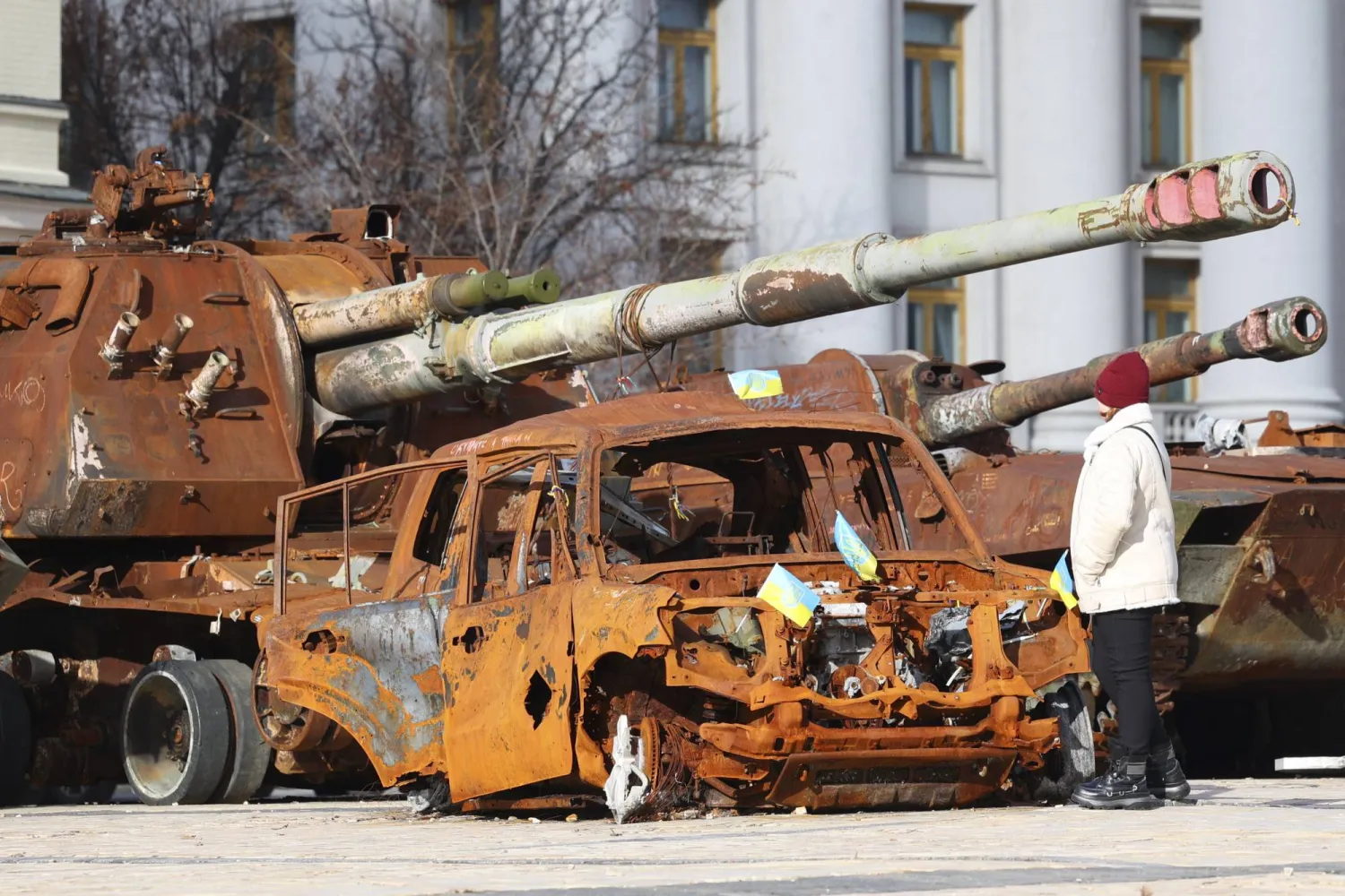 سيدة أوكرانية تشاهد سيارات روسية محترقة معروضة في ساحة ميخائيليفسكا بكييف (إ.ب.أ)