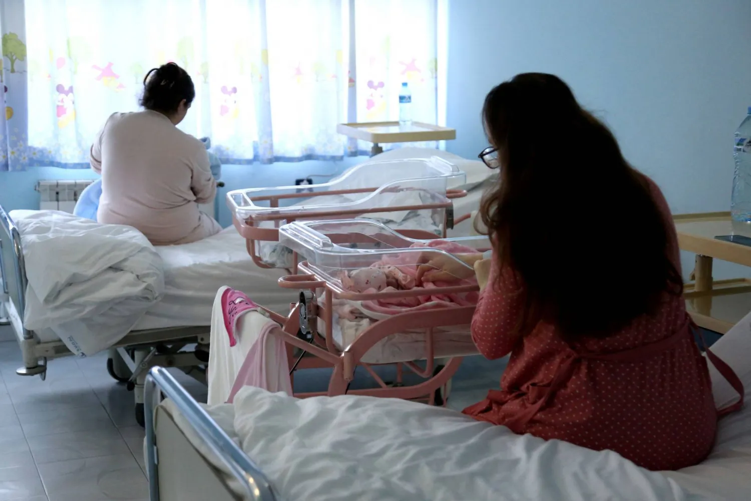 سيدة تنظر إلى مولودها الجديد في أحد مستشفيات تيرانا (أ.ف.ب)