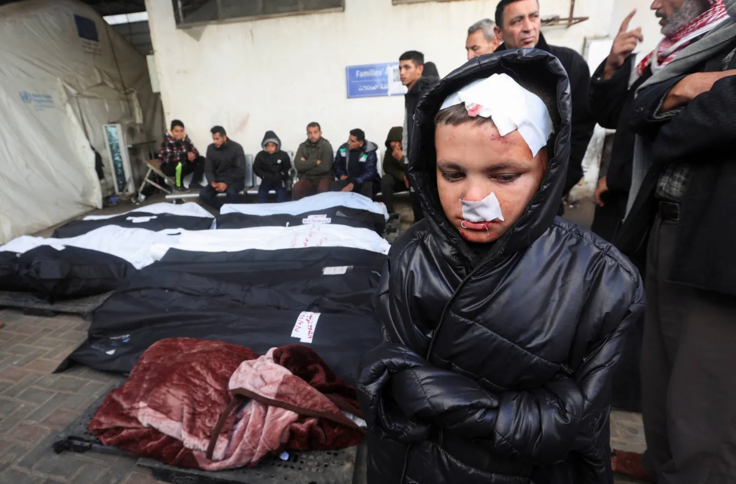 صبي فلسطيني أُصيب في غارة إسرائيلية يقف بالقرب من جثث الفلسطينيين في مستشفى أبو يوسف النجار في رفح بجنوب قطاع غزة (رويترز)