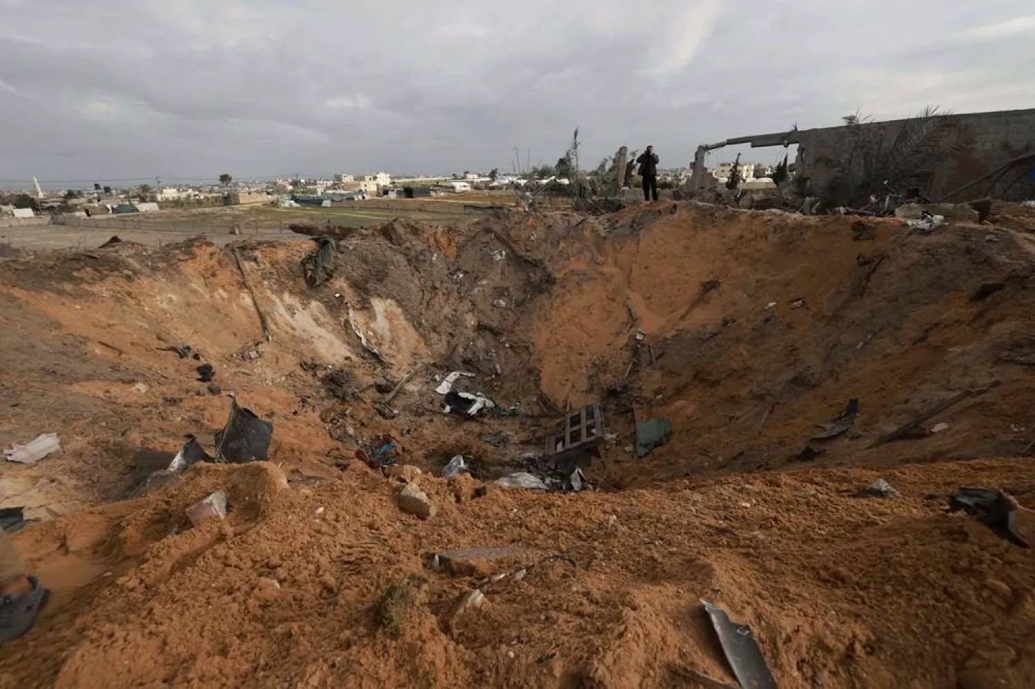A Palestinian stands next to a huge crater in Rafah on February 18, 2024, following overnight Israeli air strikes on the southern Gaza Strip border city amid ongoing battles between Israel and the Palestinian Hamas movement. (AFP)