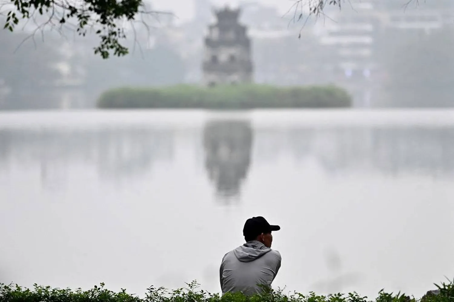 A man sits on the edge of Hoan Kiem lake in Hanoi on March 4, 2024. (AFP)