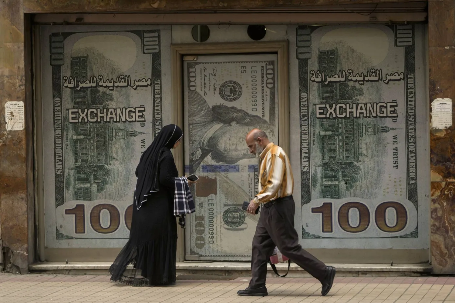 مصريون يسيرون أمام مكتب صرافة في القاهرة الأربعاء 6 مارس 2024 (أ.ب)