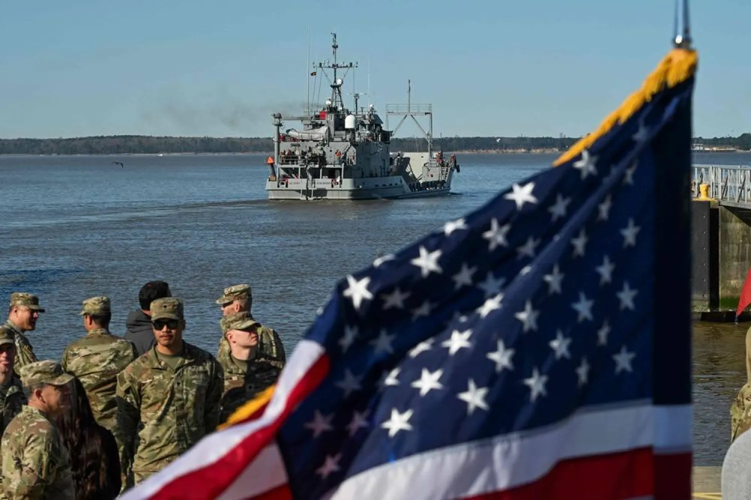 US Army soldiers stand near a US flag as the USAV Wilson Wharf sails away from the pier of the Joint Base Langley-Eustis in Virginia on March 12, 2024 during a media preview of the 7th Transportation Brigade deployment in Hampton, Virginia, on March 12, 2024. (AFP)