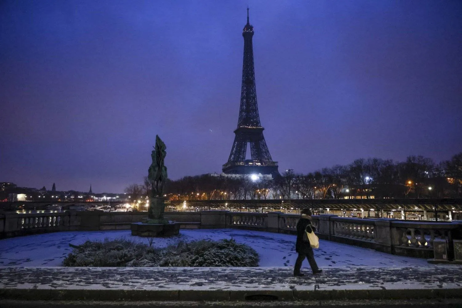 FILE - A woman walks to a bridge in front of the Eiffel Tower after snowfalls, Jan. 18, 2024 in Paris. (AP Photo/Thomas Padilla, File)
