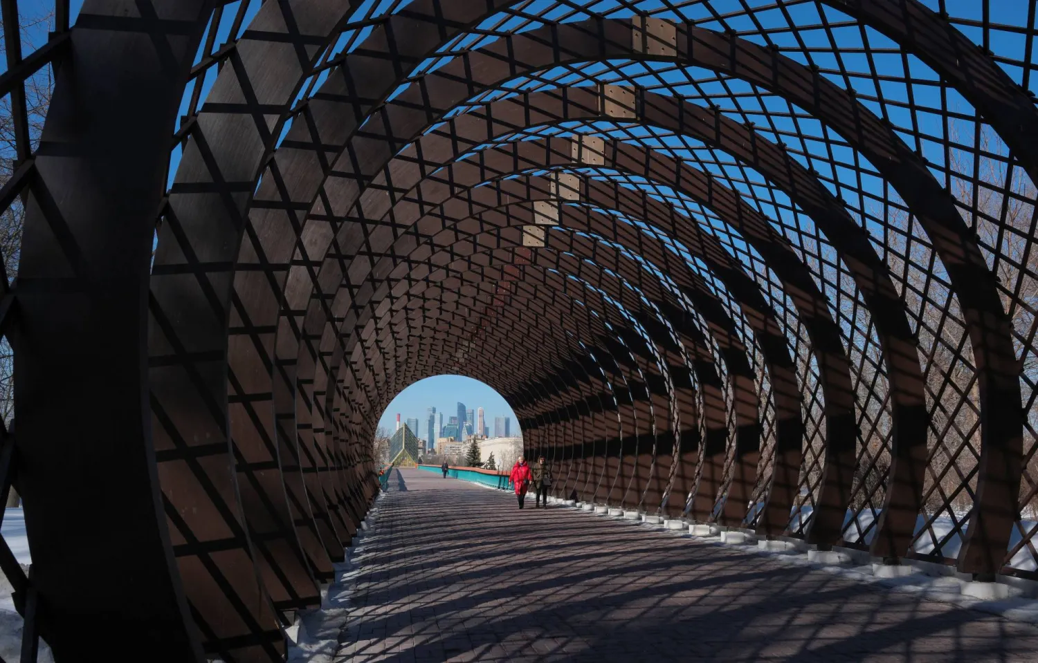 Pedestrians walk through a decorative tunnel with the backdrop of skyscrapers of Moscow International Business Center, also known as Moskva-City, on a sunny day in Moscow, Russia March 13, 2024.  REUTERS/Shamil Zhumatov