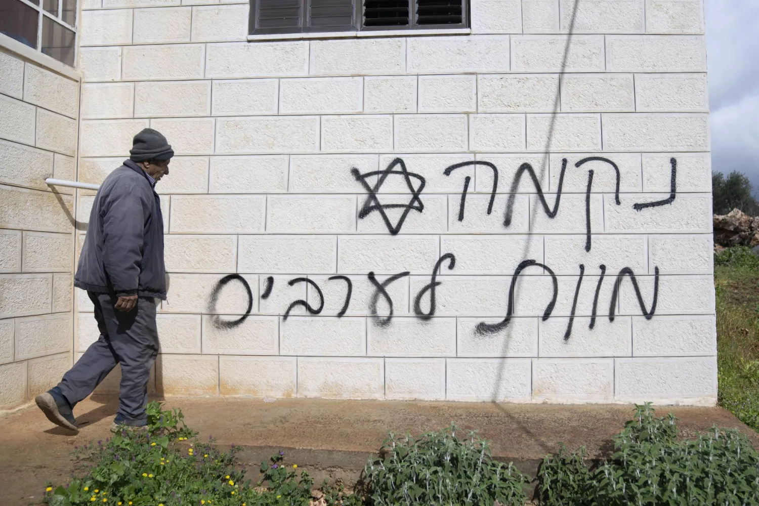 FILE - A man looks at graffiti that reads, in Hebrew, "revenge, death to Arabs," allegedly sprayed by Jewish West Bank settlers in the Palestinian West Bank village of Turmus Ayya, Feb. 18, 2024. (AP Photo/Nasser Nasser, File)