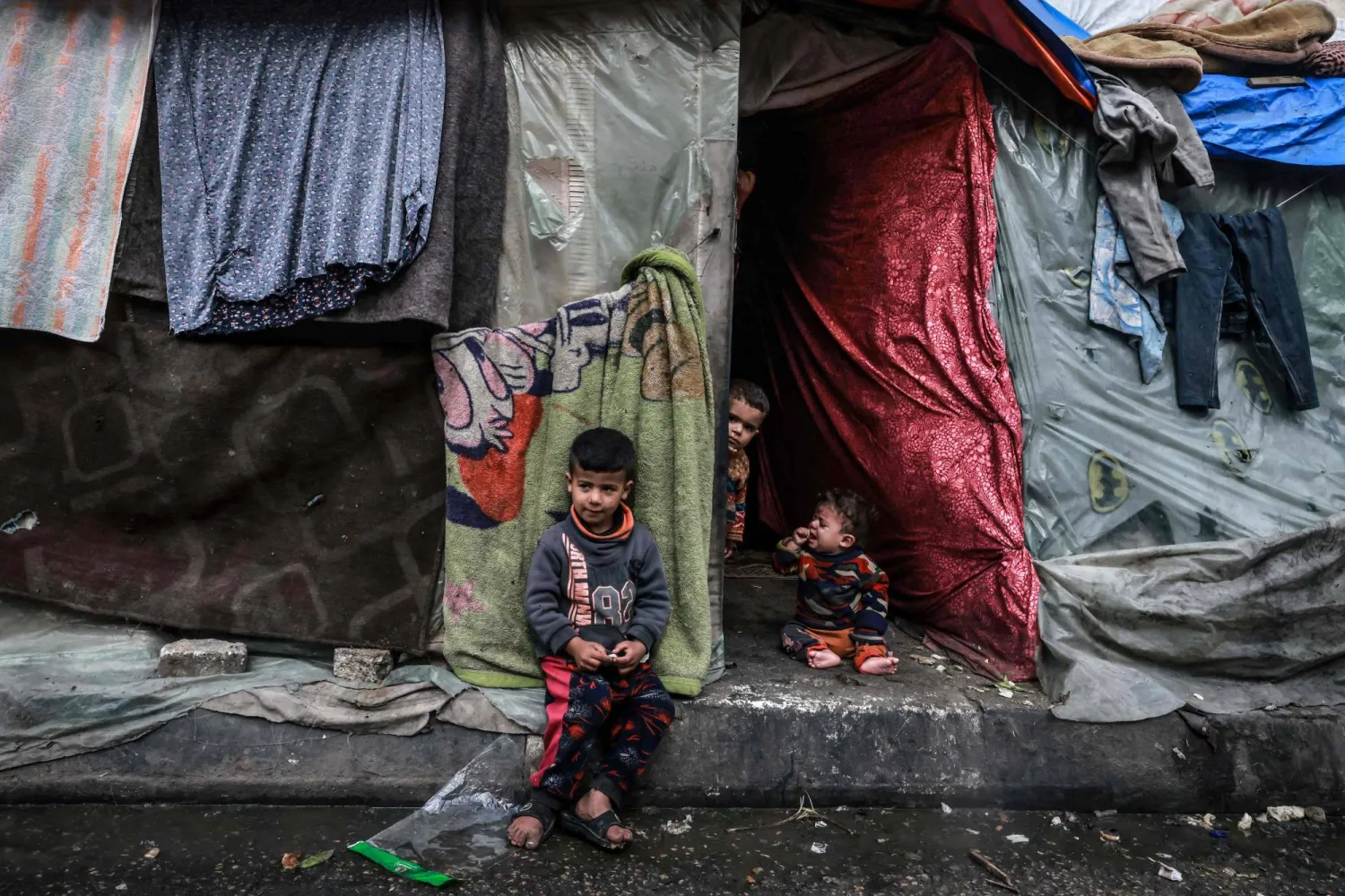 Displaced Palestinian children wait in front of their makeshift tent at a camp beside a street in Rafah on March 14, 2024. (Photo by Mohammed ABED / AFP)