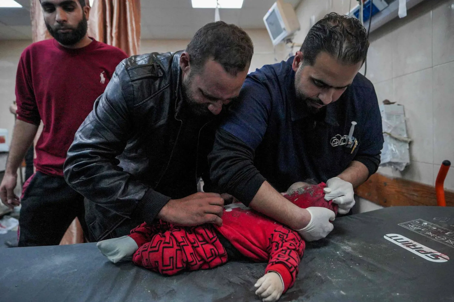 أطباء فلسطينيون يفحصون طفلاً رضيعاً جرى انتشاله من تحت أنقاض منزل تعرّض للقصف في دير البلح (أ.ف.ب)
