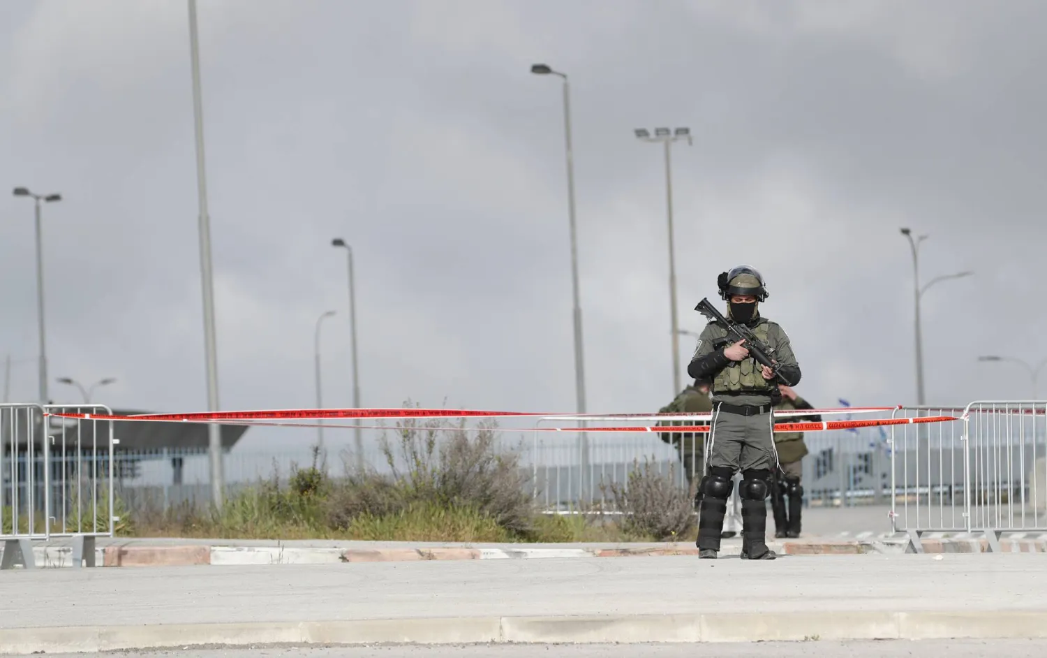 جندي إسرائيلي مسلح يراقب الفلسطينيين الذين ينتظرون عند حاجز قلنديا بين الضفة الغربية والقدس (إ.ب.أ)