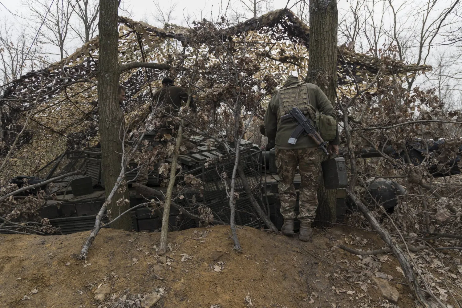 جنود من اللواء الميكانيكي الـ24 للقوات البرية الأوكرانية يقفون بجوار دبابة مخفية في موقعهم على خط المواجهة بمنطقة دونيتسك (إ.ب.أ)