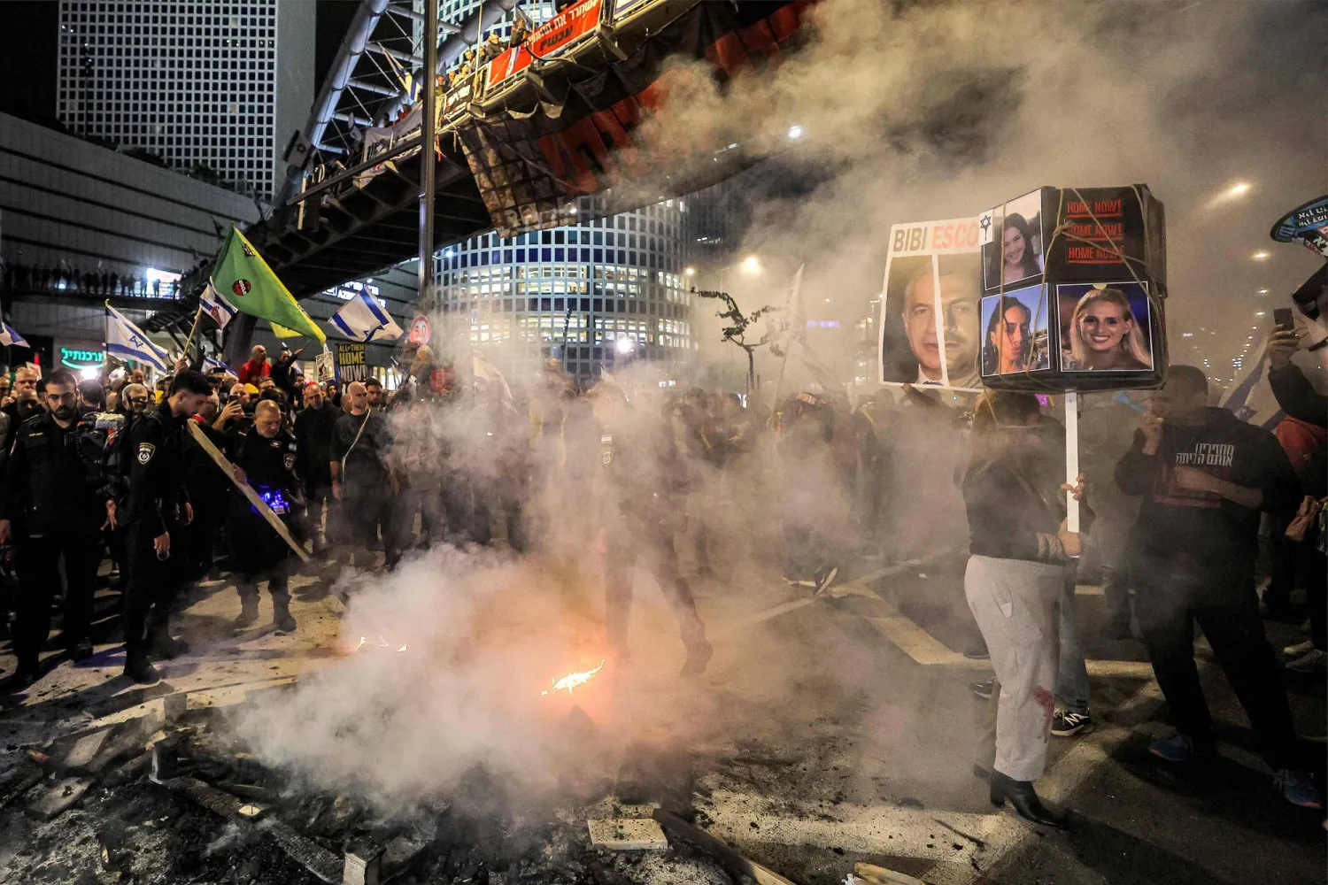 عناصر الشرطة الإسرائيلية يطفئون ناراً أشعلها نشطاء يساريون لسد طريق خلال مظاهرة مناهضة للحكومة في تل أبيب مساء السبت (أ.ف.ب)