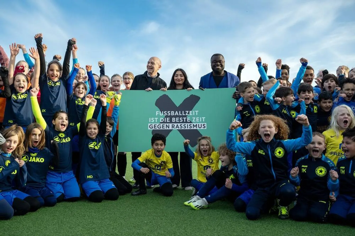 18 March 2024, Berlin: DFB President Bernd Neuendorf (C), Minister of State Reem Alabali-Radovan (SPD), Government Commissioner for Anti-Racism, and former national soccer player Gerald Asamoah, stand on the sports field next to youth players from Steglitz Football Club Star 1900 e.v. at the launch of the DFB's anti-racism campaign and hold a poster with the campaign motto "Football time is the best time against racism". (dpa) 