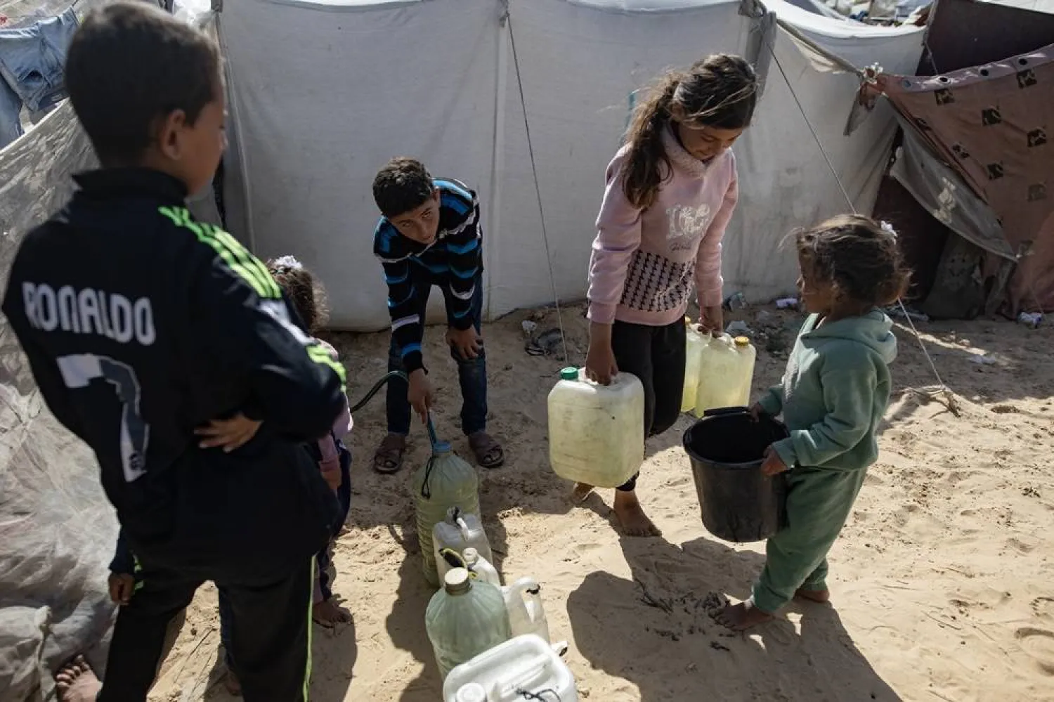 Internally displaced Palestinian children fill containers with water, in Khan Younis, southern Gaza Strip, 21 March 2024. (EPA)