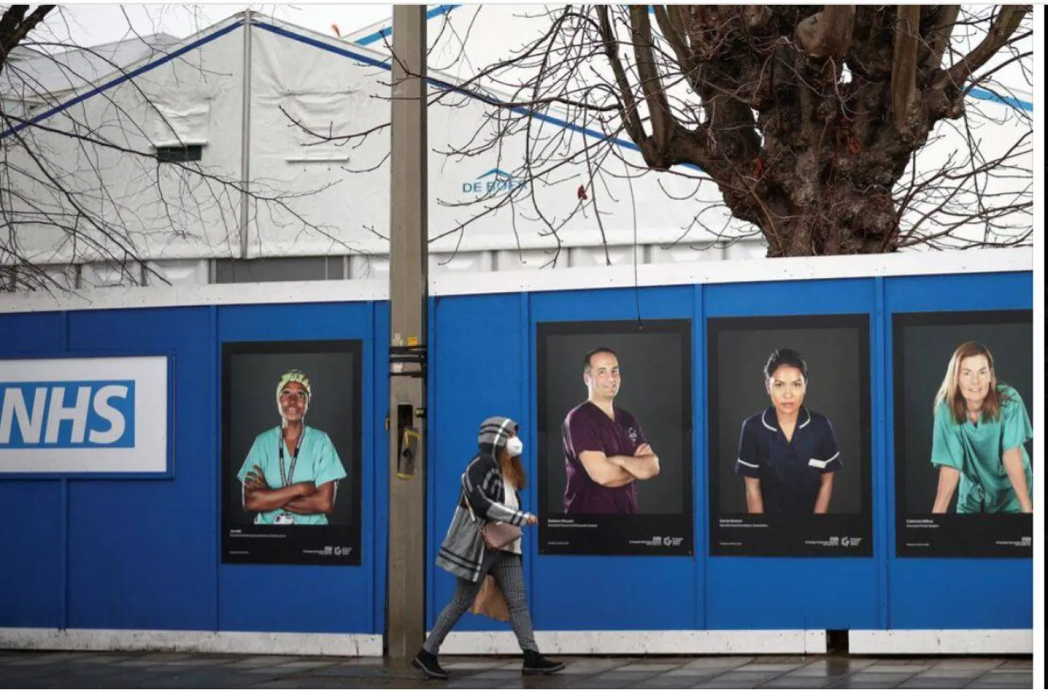 سيدة تمر أمام صور العاملين بالخدمة الصحية الوطنية المعروضة على لوحات خارج مستشفى ميداني مؤقت في مستشفى سانت جورج بلندن خلال وباء كورونا عام 2022 (رويترز)