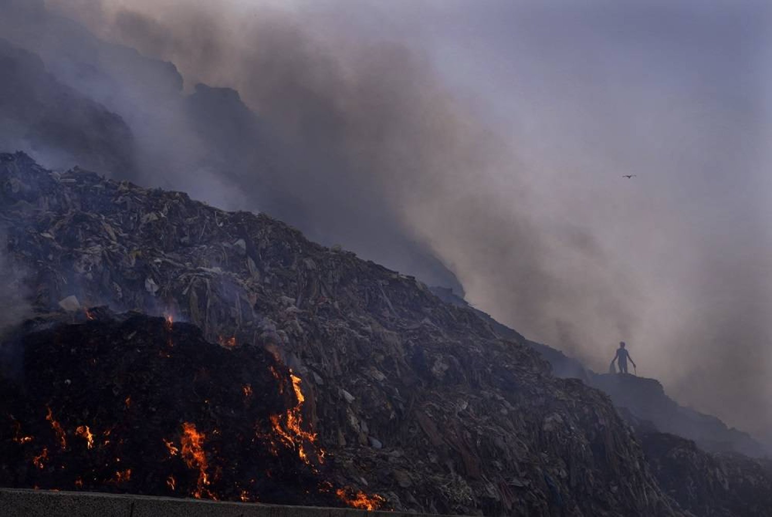 A person picks through trash for reusable items as a fire rages at the Bhalswa landfill in New Delhi, April 27, 2022. (AP)