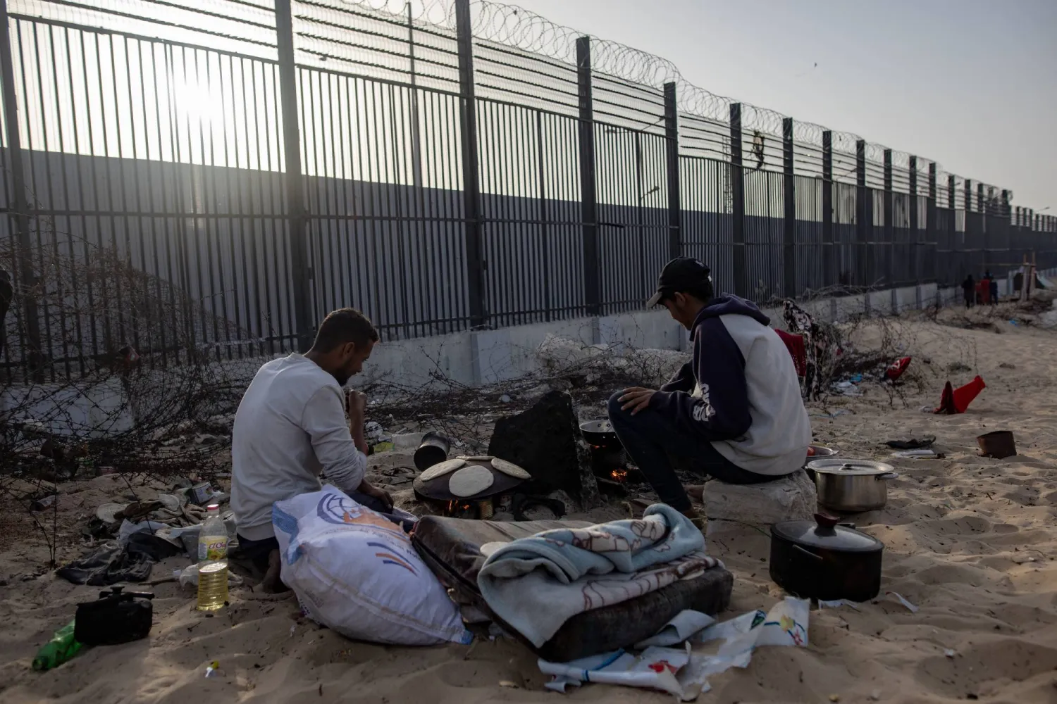 نازحون فلسطينيون يجلسون قرب الجدار الحدودي مع مصر (إ.ب.أ)