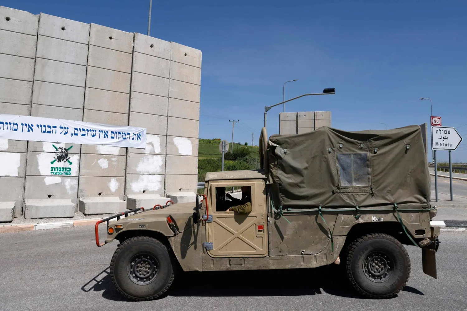 آلية عسكرية إسرائيلية تسير قرب جدار إسمنتي إسرائيلي في كريات شمونة قرب الحدود مع جنوب لبنان (أ.ف.ب)