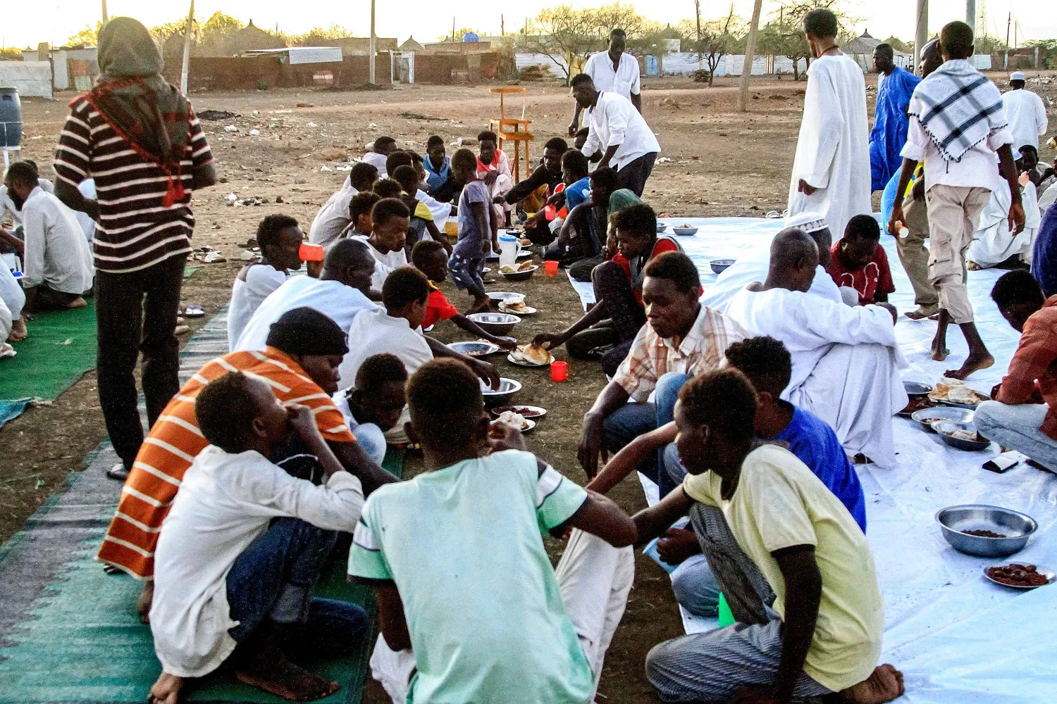 People displaced by the ongoing conflict in Sudan break their fast together during the Muslim holy month of Ramadan in a mass "Iftar" meal provided by a charity organization, at the Huri camp for the displaced, south of Gedaref in eastern Sudan, on March 29, 2024. (Photo by Ebrahim Hamid / AFP)