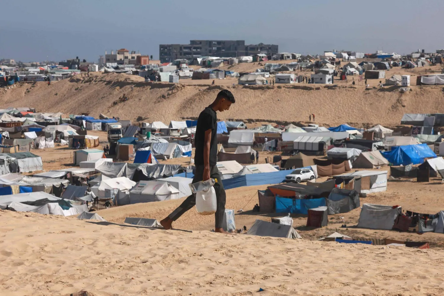 A Palestinian man ferries water at a makeshift camp for displaced people in Rafah in the southern Gaza Strip on April 4, 2024. (Photo by MOHAMMED ABED / AFP)
