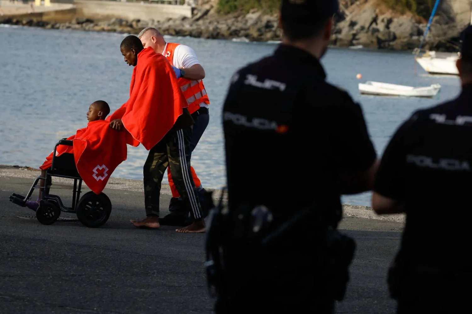 A Red Cross volunteer transfers two migrants to a tent to be attended after disembarking from a Spanish coast guard vessel, in the port of Arguineguin, on the island of Gran Canaria, Spain, April 4, 2024. REUTERS/Borja Suarez