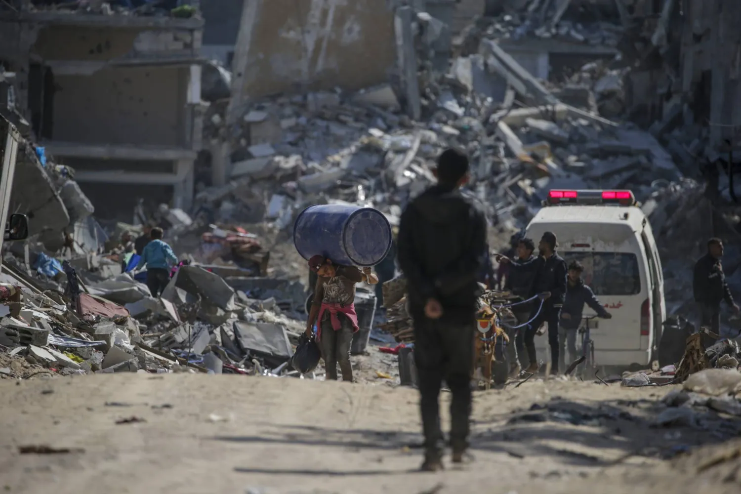فلسطينيون يسيرون بين الأنقاض بمنطقة مدمرة في خان يونس (إ.ب.أ)