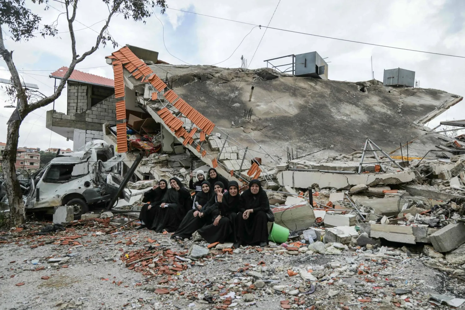 Residents of the southern Lebanese village of Aita al-Shaab pose for a picture in front of a house which was destroyed by previous Israeli fire, as they visit their deserted village on the occasion of a funeral of a Hezbollah fighter, on April 9, 2024, in southern Lebanon near the border with Israel. (Photo by Hasan FNEICH / AFP)