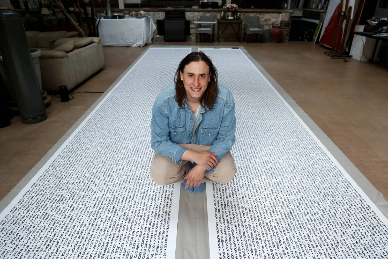 French artist Baptiste Chebassier poses in the middle of a part of his artwork, made from rolls of recycled paper on which names of 30,249 Olympic medallists will be written, at the Chebassier workshop in Saint-Ouen, near Paris, France, April 5, 2024. REUTERS/Noemie Olive