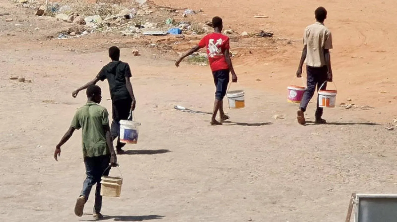 فتيان يحملون دلاء مملوءة بالماء في أحد شوارع الخرطوم  (أ.ف.ب)
