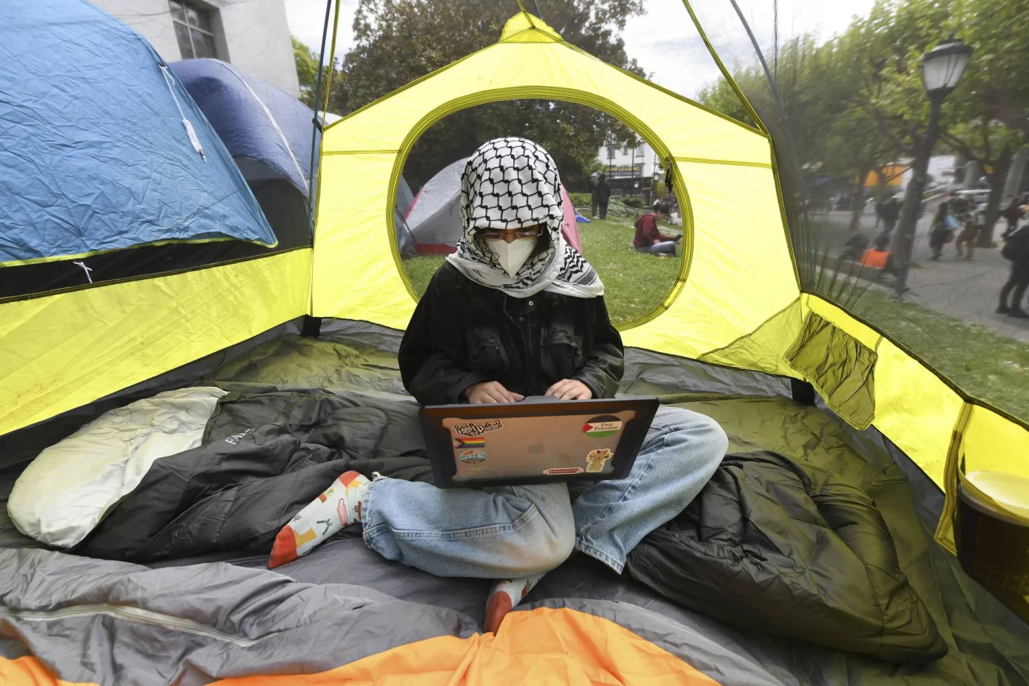 الطالبة إيسا تعمل على جهاز كومبيوتر داخل إحدى الخيام داخل جامعة كاليفورنيا - بيركلي (أ.ب)