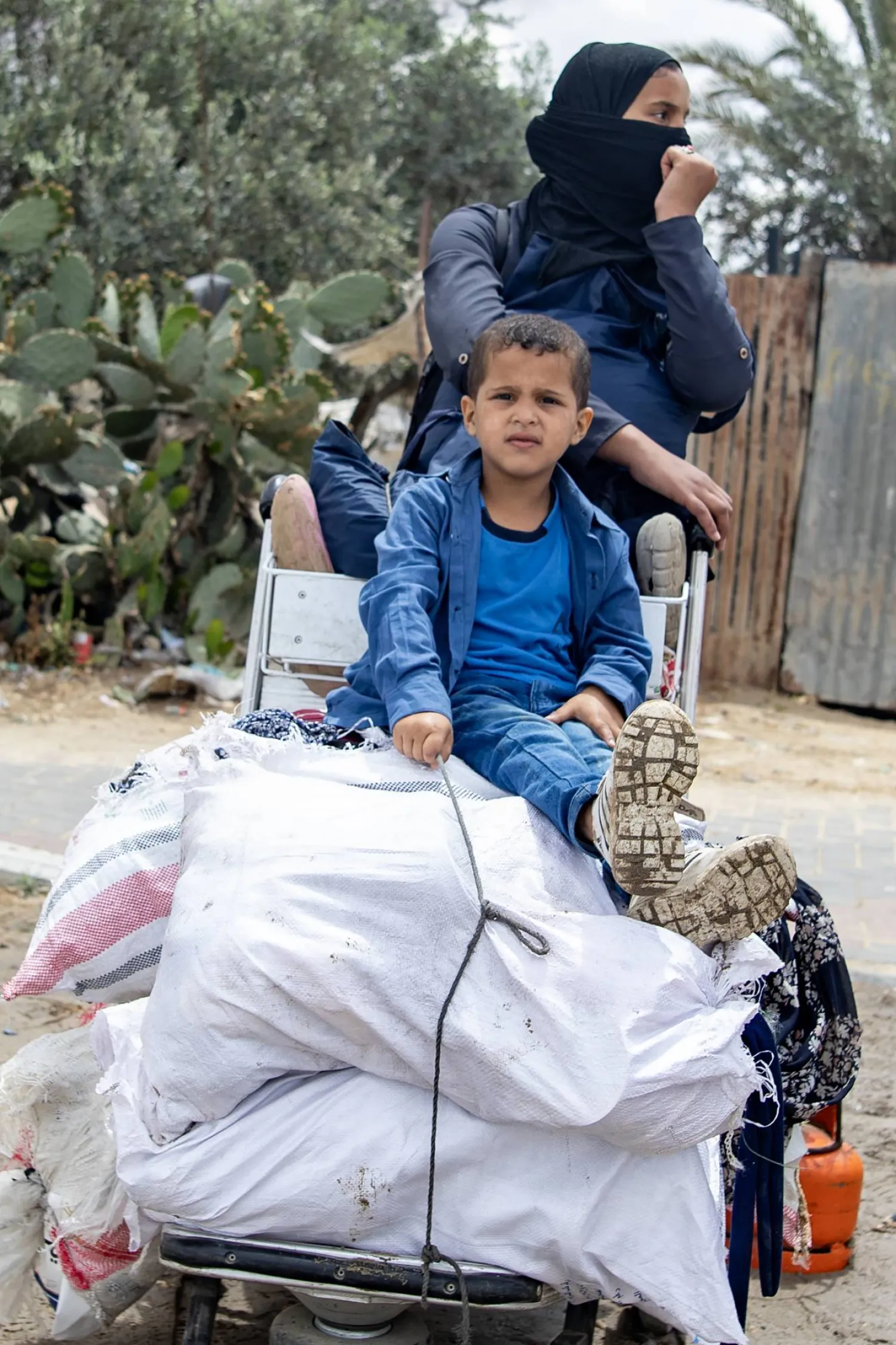 طفل برفقة أمه يستريحان من السير في رحلة النزوح الجديدة هرباً من العدوان الإسرائيلي (إ.ب.أ)