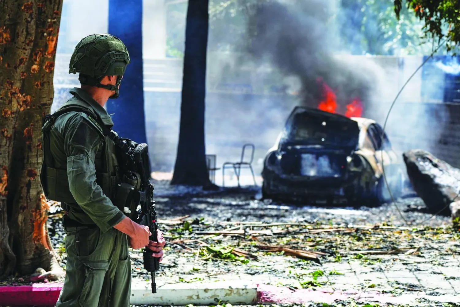 جندي إسرائيلي يراقب نيران اندلعت بسيارة في كريات شمونة إثر صواريخ انطلقت من جنوب لبنان (رويترز)