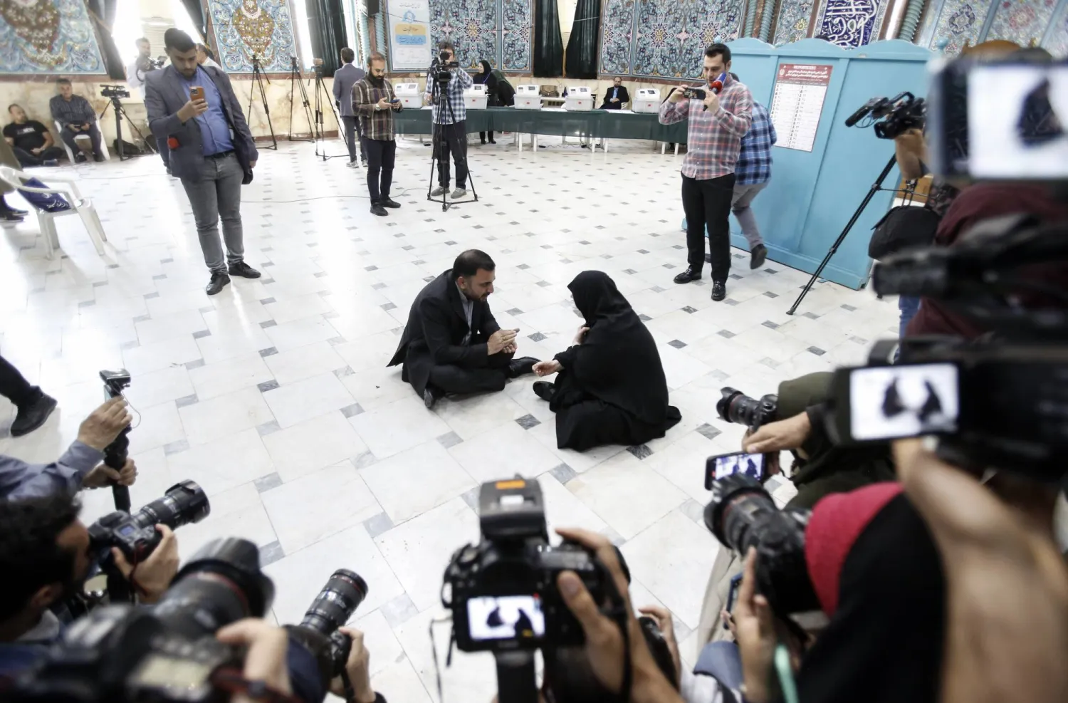 وزير تكنولوجيا المعلومات الإيراني عيسى زارع پور جالساً على أرضية مركز انتخابي ومتحدثاً مع ناخبة إيرانية (إ.ب.أ)