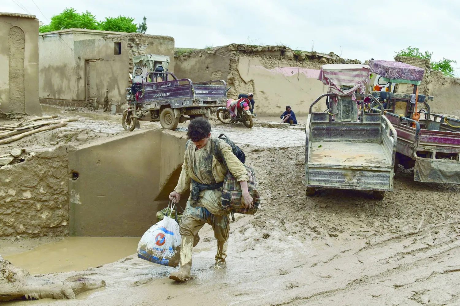 An Afghan man carries his belongings as he walks through a mud covered street following a flash flood after a heavy rainfall in Laqiha village of Baghlan-i-Markazi district in Baghlan province on May 11, 2024. (Photo by AFP)
