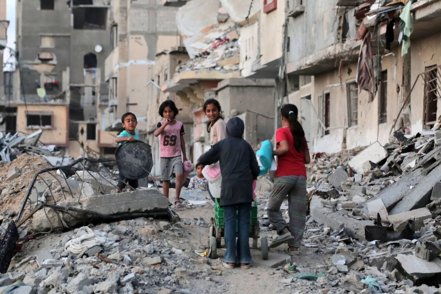 أطفال فلسطينيون نازحون يسيرون على طول شارع مليء بالحطام لجلب المياه في خان يونس بجنوب قطاع غزة (أ.ف.ب)