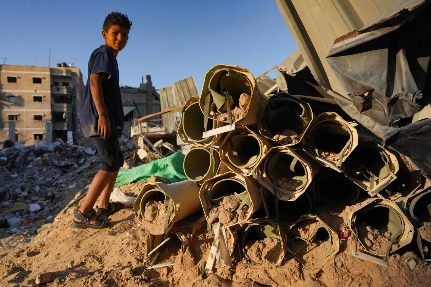 طفل فلسطيني يقف بجوار قذائف إسرائيلية فارغة في خان يونس بجنوب قطاع غزة (ا.ف.ب)