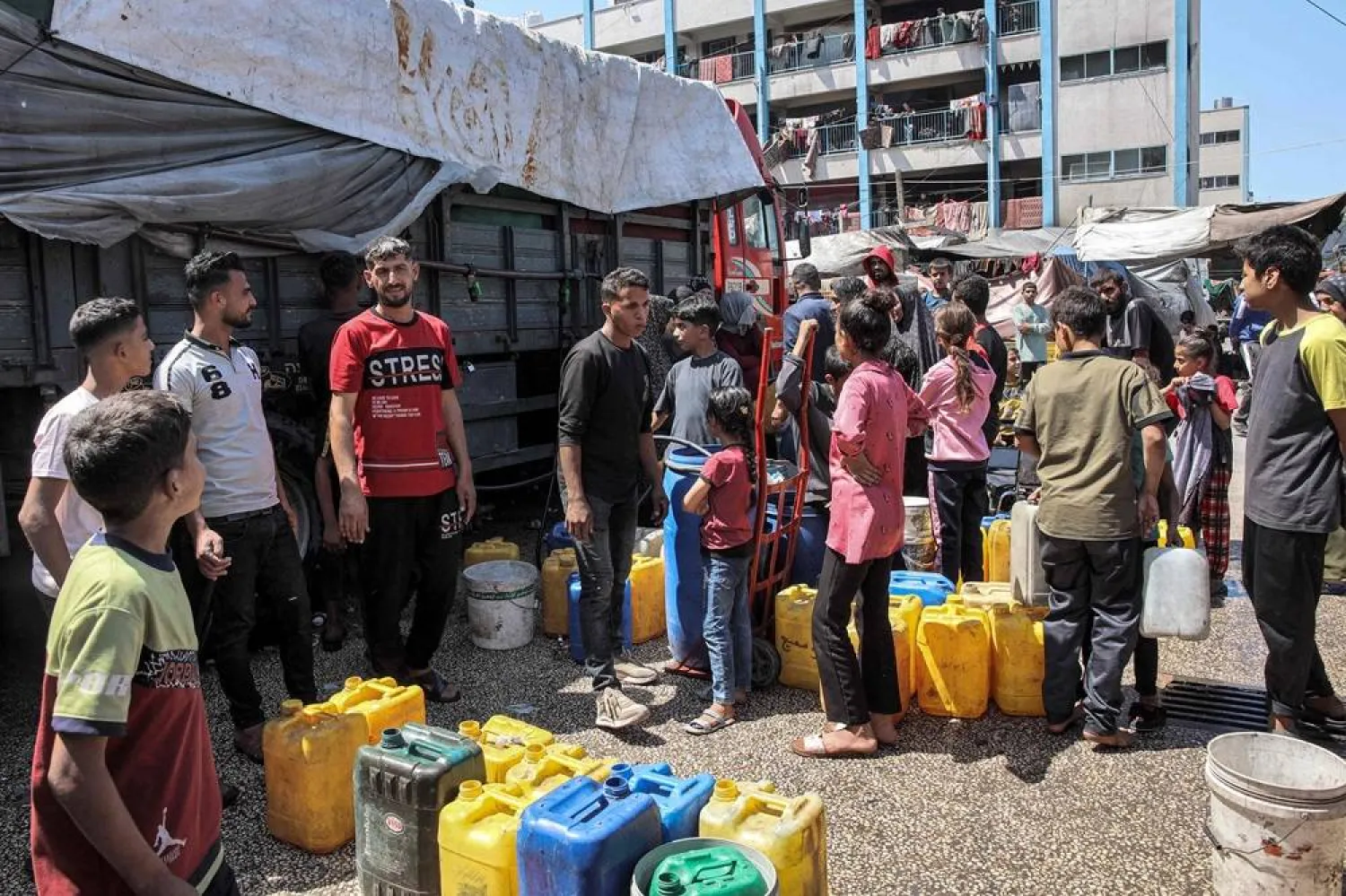 Youths gather with jerrycans to fill up water from a tanker truck in the yard of a school of the United Nations Relief and Works Agency for Palestine Refugees in the Near East (UNRWA), housing Palestinians displaced by the ongoing conflict in the Gaza Strip between Israel and Hamas, in Jabalia in the north of the Palestinian territory on May 14, 2024. (AFP) 
