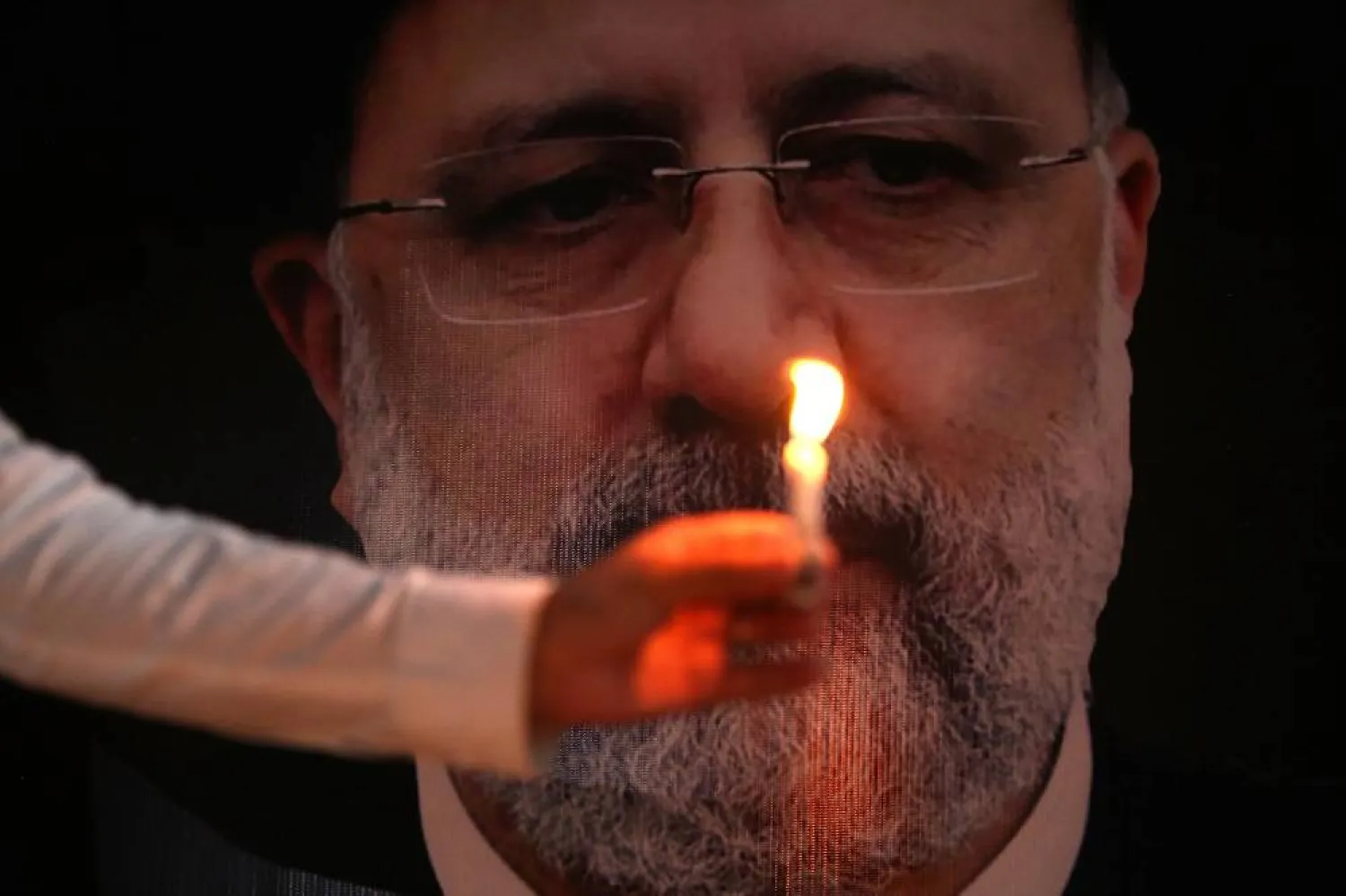 A person holds a candle in front of photo of Iran's late president Ebrahim Raisi, at the Khana-e-Farhang Iranian culture center in Peshawar, Pakistan, 23 May 2024. (EPA)