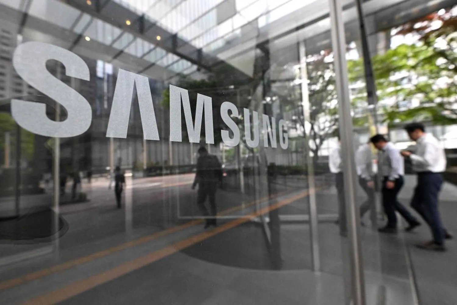 People walk past the Samsung logo displayed on a glass door at the company's Seocho building in Seoul on April 30, 2024. (AFP)