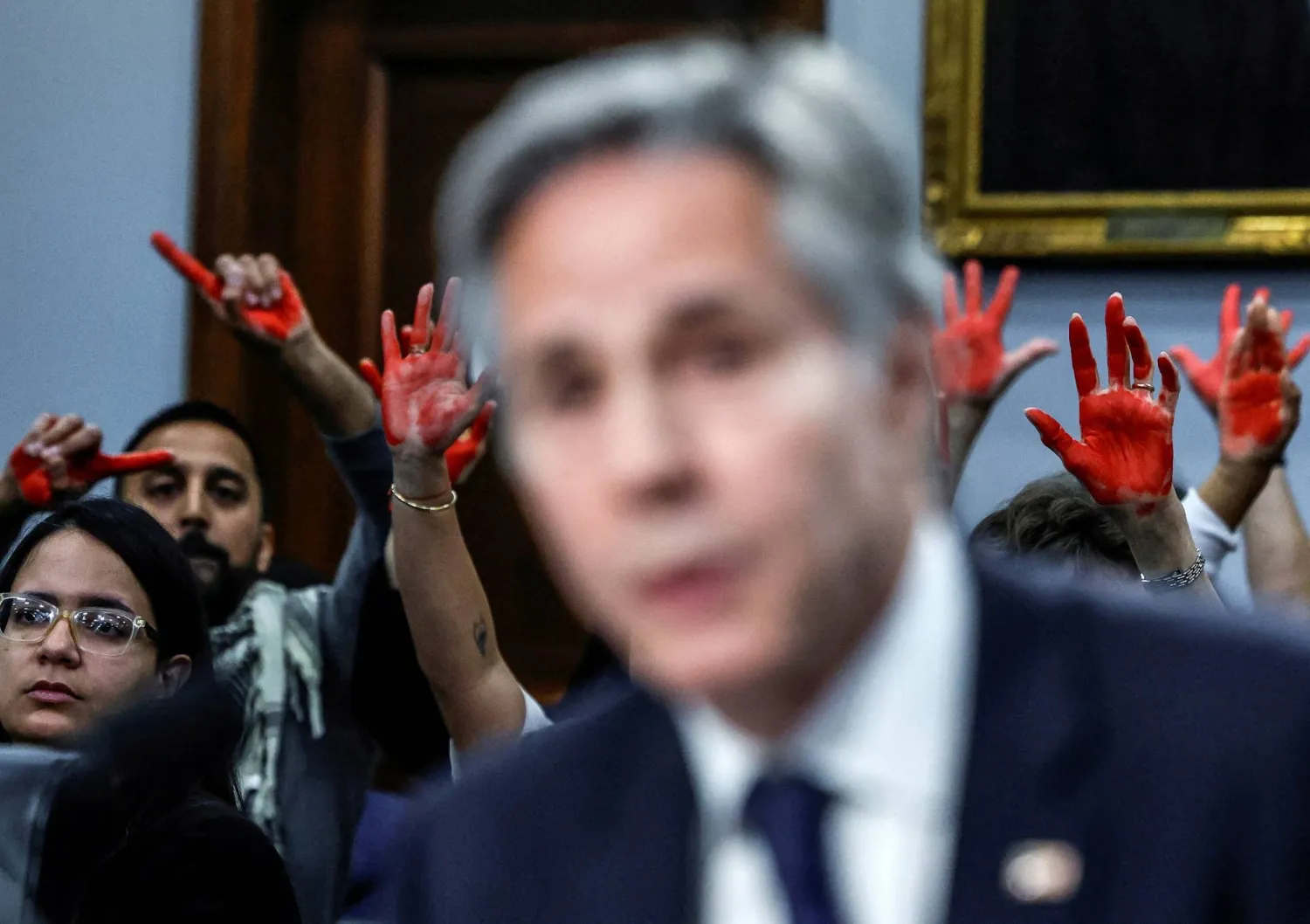 متظاهرون مؤيدون للفلسطينيين يرفعون الأيادي الحمراء بينما يدلي وزير الخارجية الأميركي أنتوني بلينكن بشهادته أمام جلسة استماع في «كابيتول هيل» بواشنطن يوم 22 مايو 2024 (رويترز)