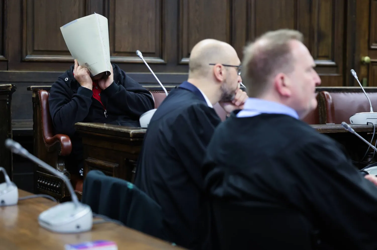 أحد المتهمين (يسار) ومحامياه توماس دومانسكي (يمين) وفيليكس دويتشر ينتظرون بدء المحاكمة في قاعة المحكمة بمبنى العدالة الجنائية... طالب ممثلو الادعاء الألمان بإصدار أحكام بالسجن على اثنين من المتهمين في أول محاكمة لأعضاء مشتبه بهم في «حزب الله» اللبناني بألمانيا (د.ب.أ )