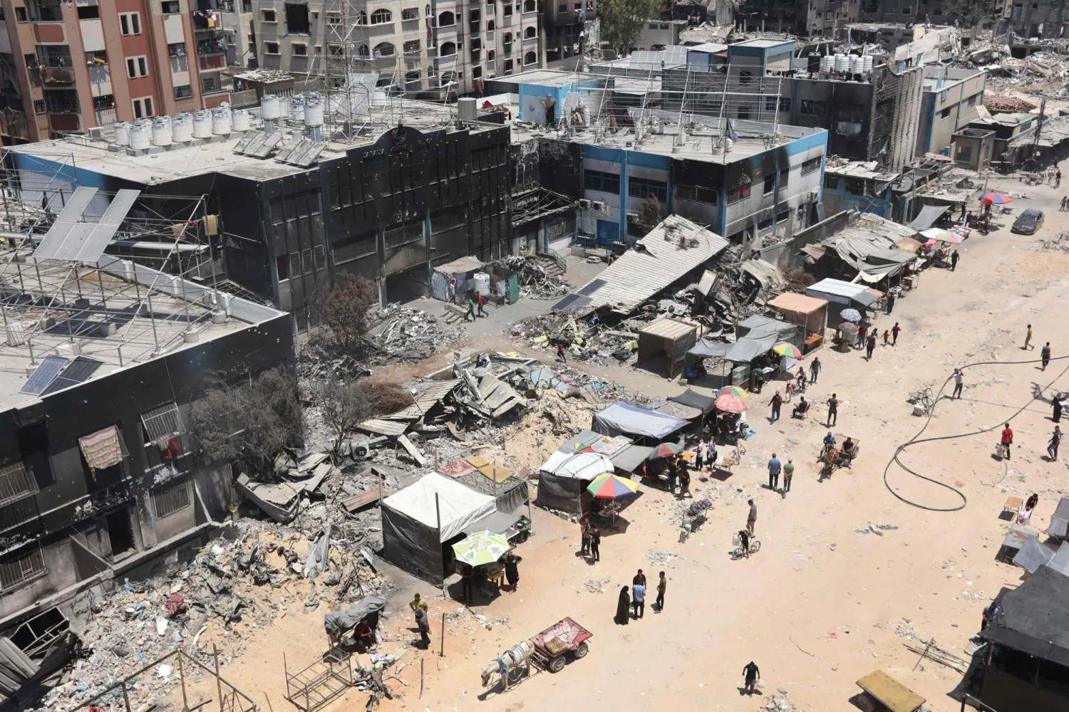 أقام الباعة أكشاك الطعام والسلع خارج الأنقاض المحترقة لمبنى وكالة الأمم المتحدة لإغاثة وتشغيل لاجئي فلسطين في الشرق الأدنى (الأونروا) (أ.ف.ب)