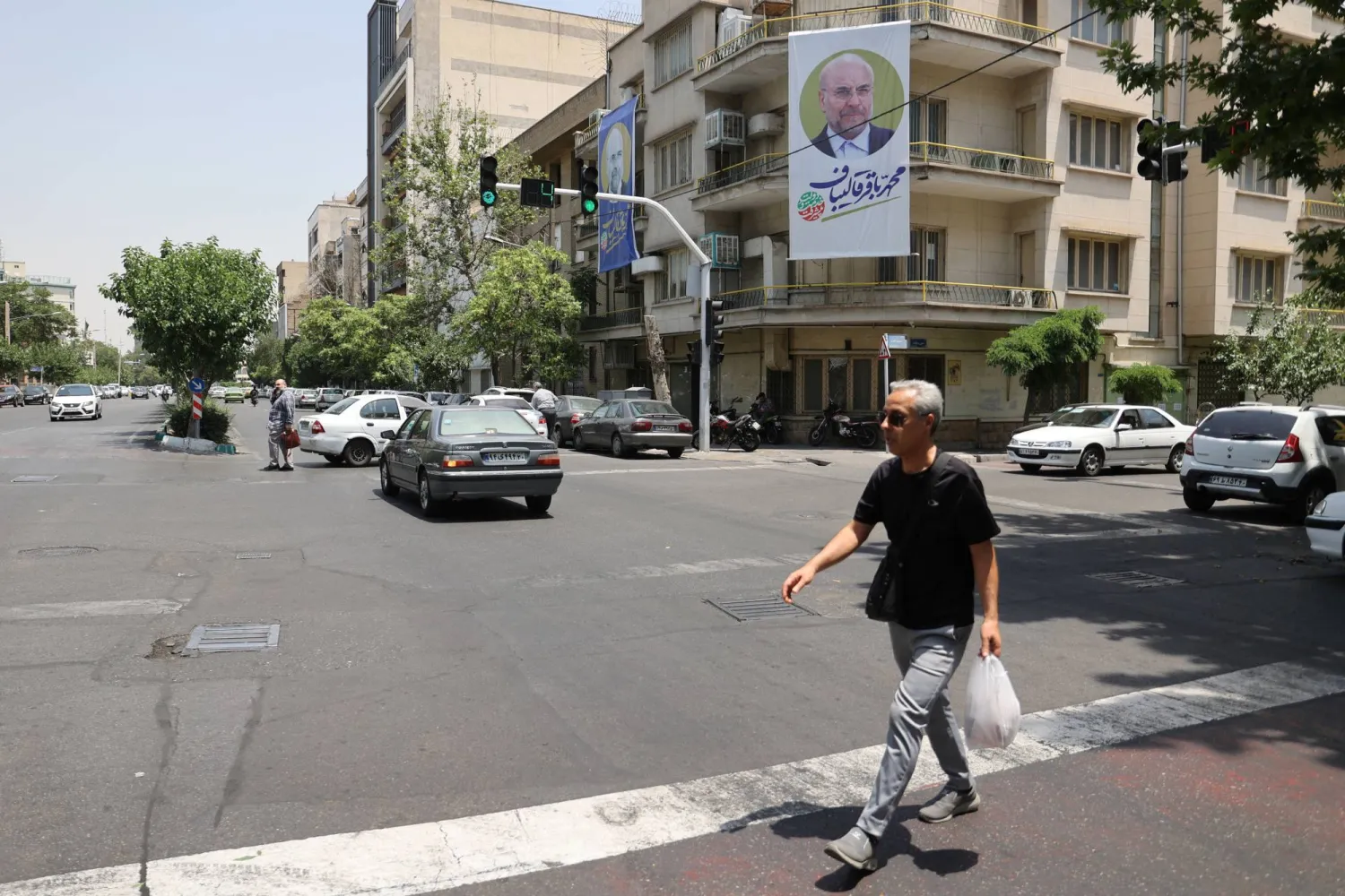 إيراني يمر بجوار مبنى رفعت عليه لافتة قاليباف خلال حملة الانتخابات الرئاسية اليوم (رويترز)