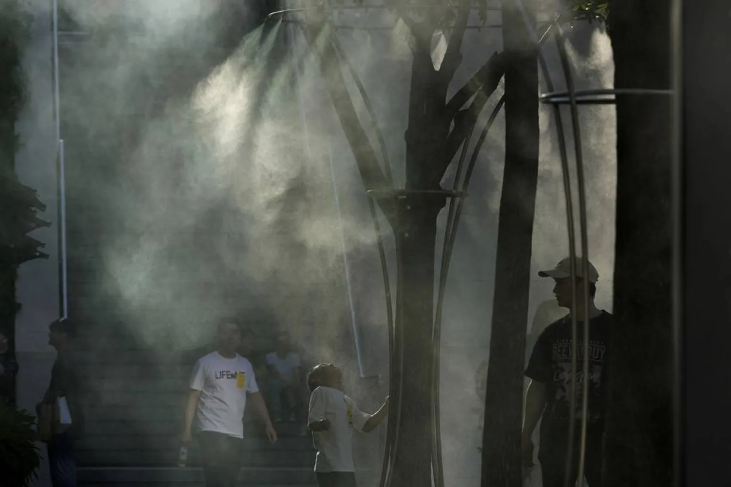  Visitors to a mall cool off near a mist machine during the summer heat in Beijing, Saturday, June 15, 2024. (AP) 