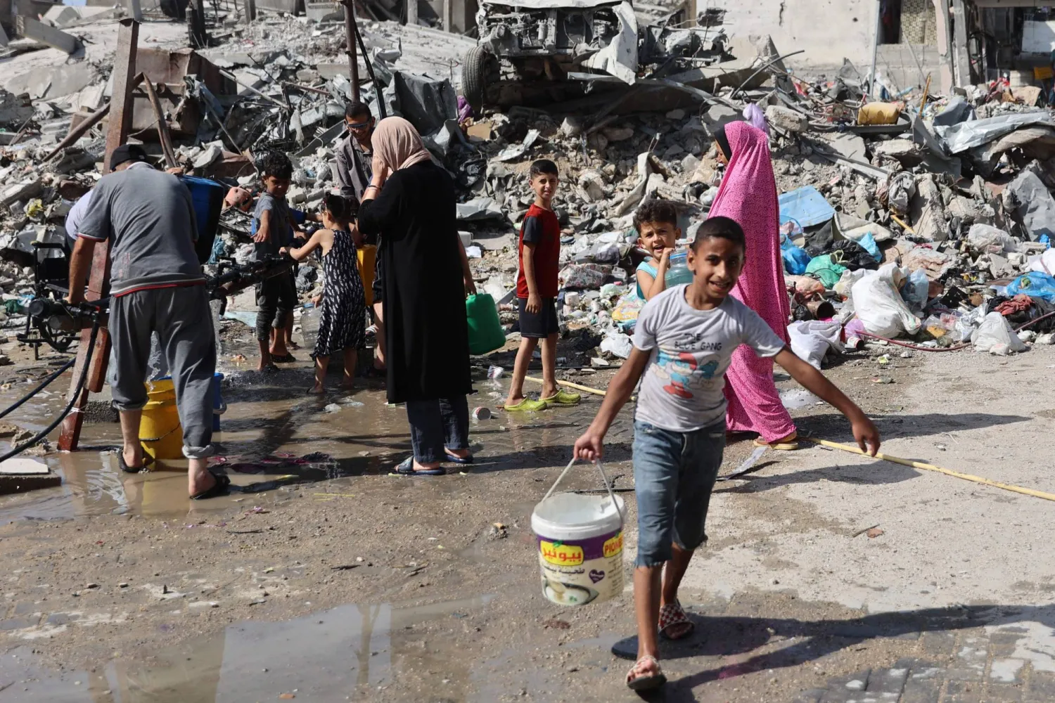 A Palestinian walks with a pail of water filled from a standpipe in the Jabalia refugee camp, in the northern Gaza Strip on June 20, 2024. (Photo by Omar AL-QATTAA / AFP)
