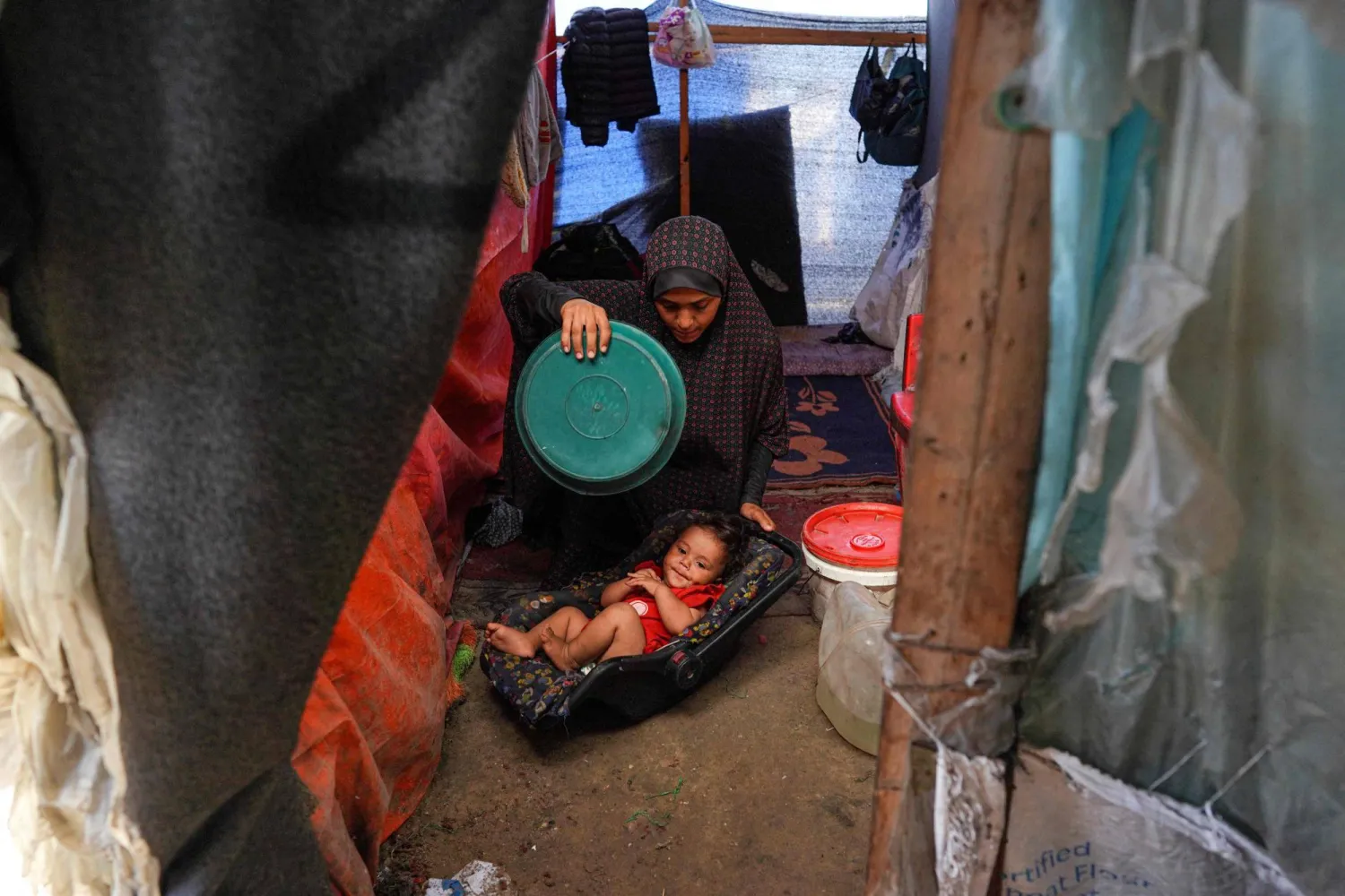 امرأة فلسطينية نازحة تستخدم طبقاً بلاستيكياً لتهوية طفلها خلال موجة الحر في دير البلح (أ.ف.ب)