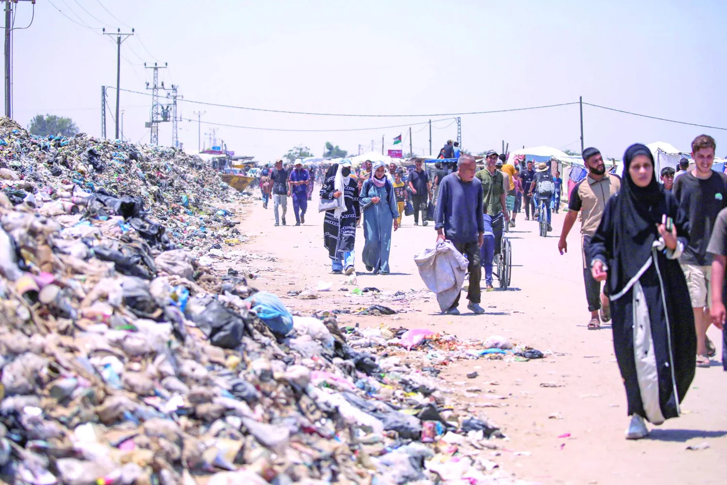 
غزيون يمشون في طريق تغطيها القاذورات بخان يونس جنوب قطاع غزة أمس (أ.ف.ب)